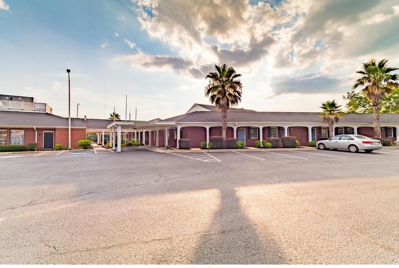 A motel with a parking lot, palm trees, and a clear sky.