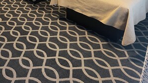 Dos camas individuales con cabeceros, una alfombra estampada, una mesita de noche con una lámpara y una puerta que da a un baño.