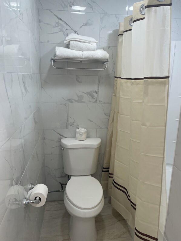 Une salle de bain avec des toilettes, des murs en marbre, un porte-serviettes avec des serviettes et un rideau de douche.