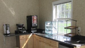 Una cocina con armarios de madera, encimera negra, cafetera, vitrina de vidrio y ventana con vistas al exterior.
