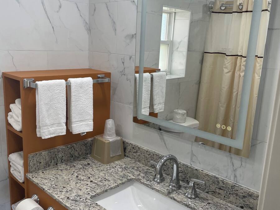 A bathroom with a marble-tiled wall, a granite countertop sink, a mirror, and a towel rack with folded towels.