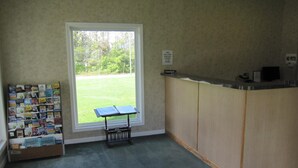Un área de recepción con un mostrador, un tablón de anuncios con postales y una ventana con vistas a zonas verdes.
