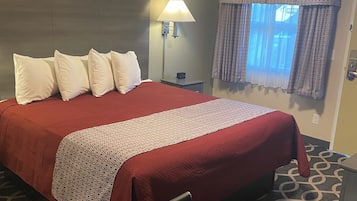 Habitación de hotel con una cama grande, una mesita de noche, una lámpara, una ventana con cortinas estampadas y una alfombra con diseño.