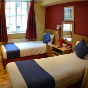 A hotel room with two beds, a bedside table with a phone and a red mug, a window with curtains, and a mirror on the wall. - Le Villé Hotel (Manchester)