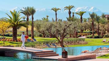A resort pool area with a person walking, palm trees, and a mountain in the background.