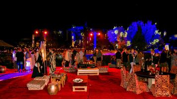 Evento formal al aire libre, con alfombra roja, mesas redondas y asientos estampados.