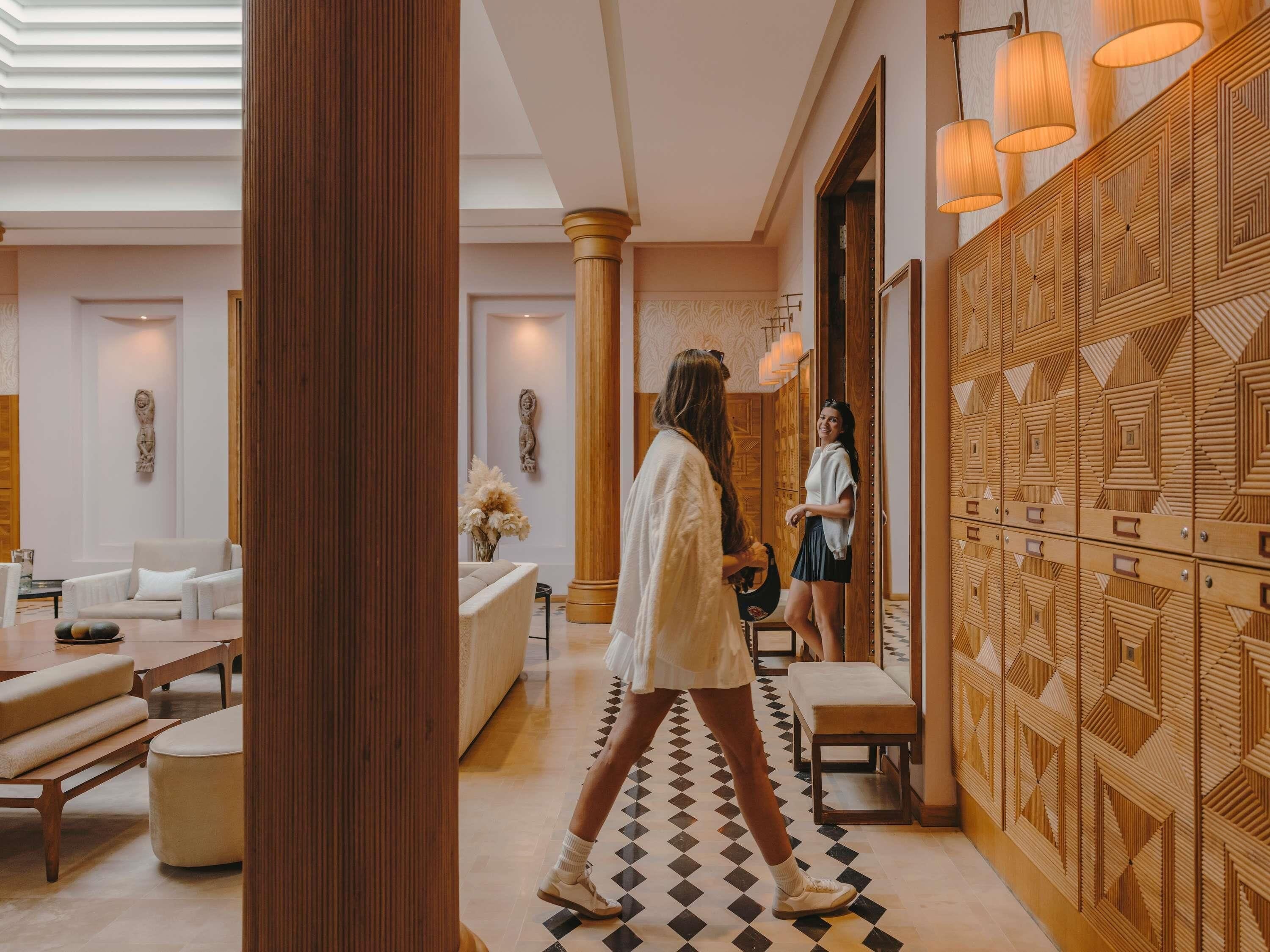 Um hall de hotel com piso xadrez, colunas de madeira e parede estampada.