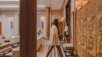 Um hall de hotel com piso xadrez, colunas de madeira e parede estampada.