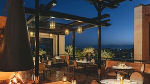 Un espacio de comedor al aire libre con mesas y sillas, una chimenea y vistas del paisaje.