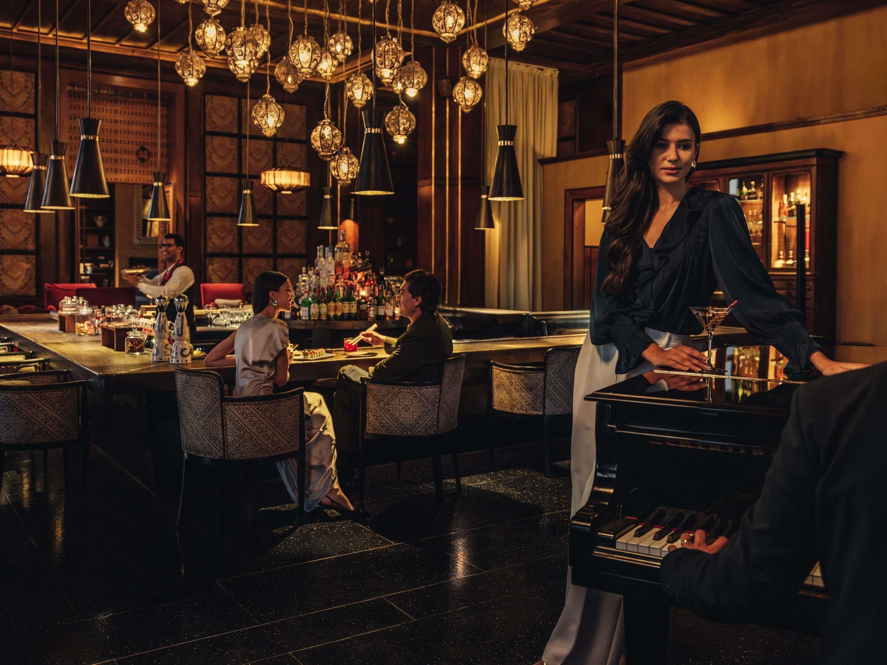 Zona de bar con diversas opciones de asientos, un cantinero y un piano.