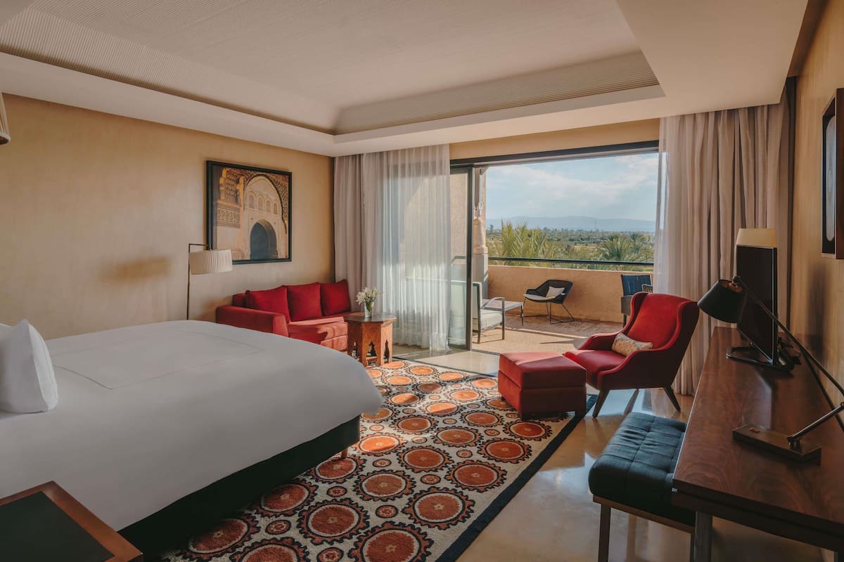 Une chambre d’hôtel avec un grand lit, un canapé, un fauteuil, une petite table, une télévision et un balcon avec vue.
