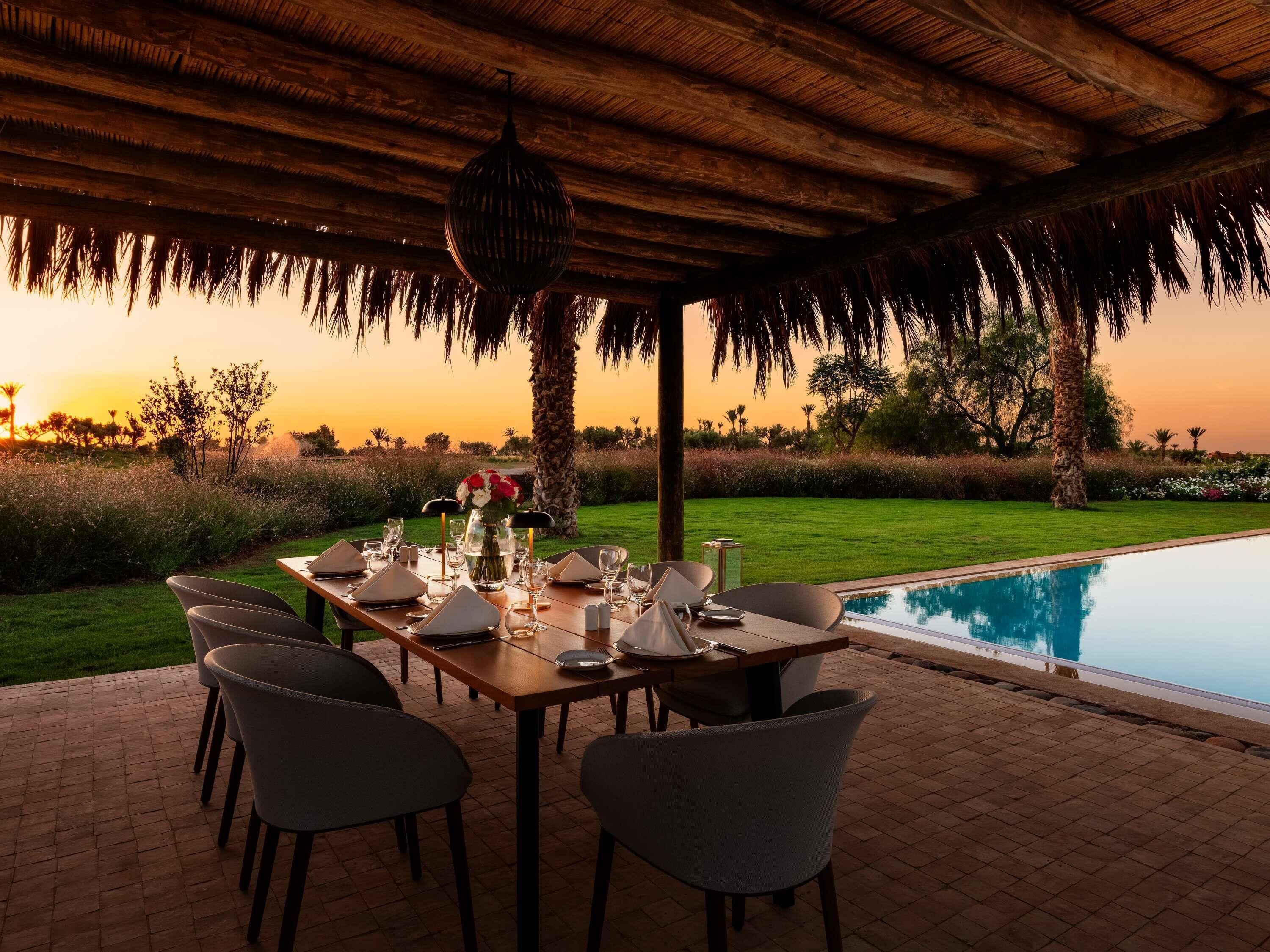 An outdoor dining area with a pool, tables set with white tablecloths, and chairs.