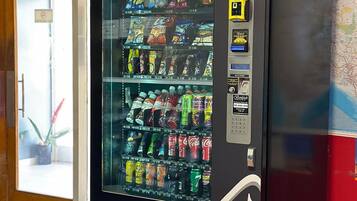 Máquina de vendas com diversos snacks e bebidas, um terminal de pagamento e um mapa na parede ao fundo.