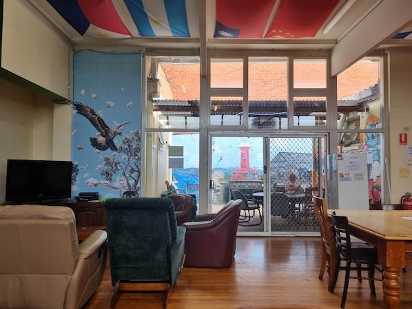 A room with a television, a sofa, a chair, a dining table, and a view of the outside through a glass door.