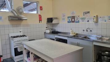 A compact kitchen with a gas stove, a microwave, a toaster, and a sink. There are various hygiene posters on the wall, and a small shelf with mugs.