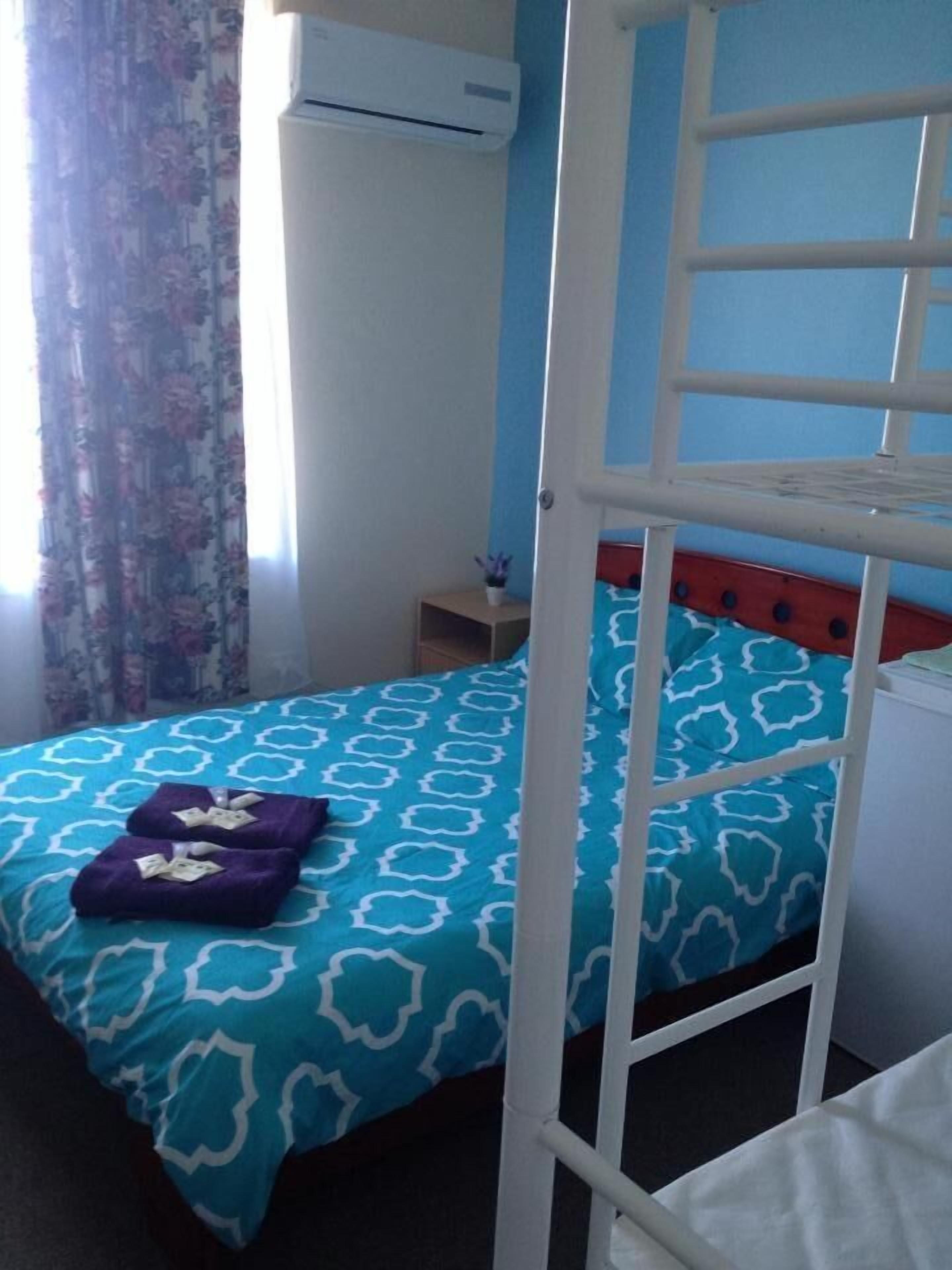 A room with a bunk bed, a small bedside table with a lamp, and a window with floral curtains.