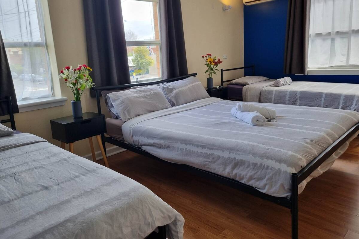 Ein Hotelzimmer mit zwei Betten, einem Fenster, einem Nachttisch und einer Vase mit Blumen.
