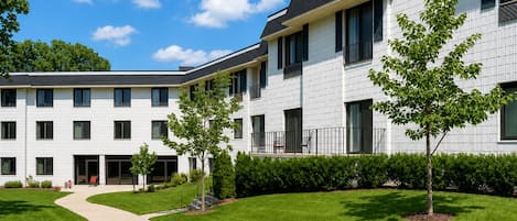 A modern multi-story building with a flat roof, large windows, and a well-maintained lawn with young trees.