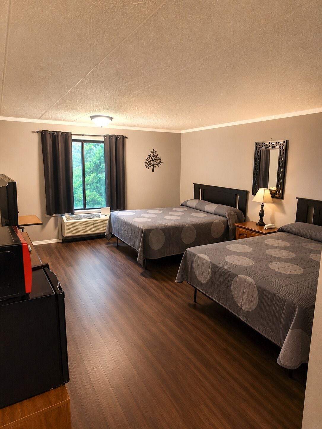 Ett hotellrum med två sängar, ett skrivbord, en TV och ett fönster med gardiner.
