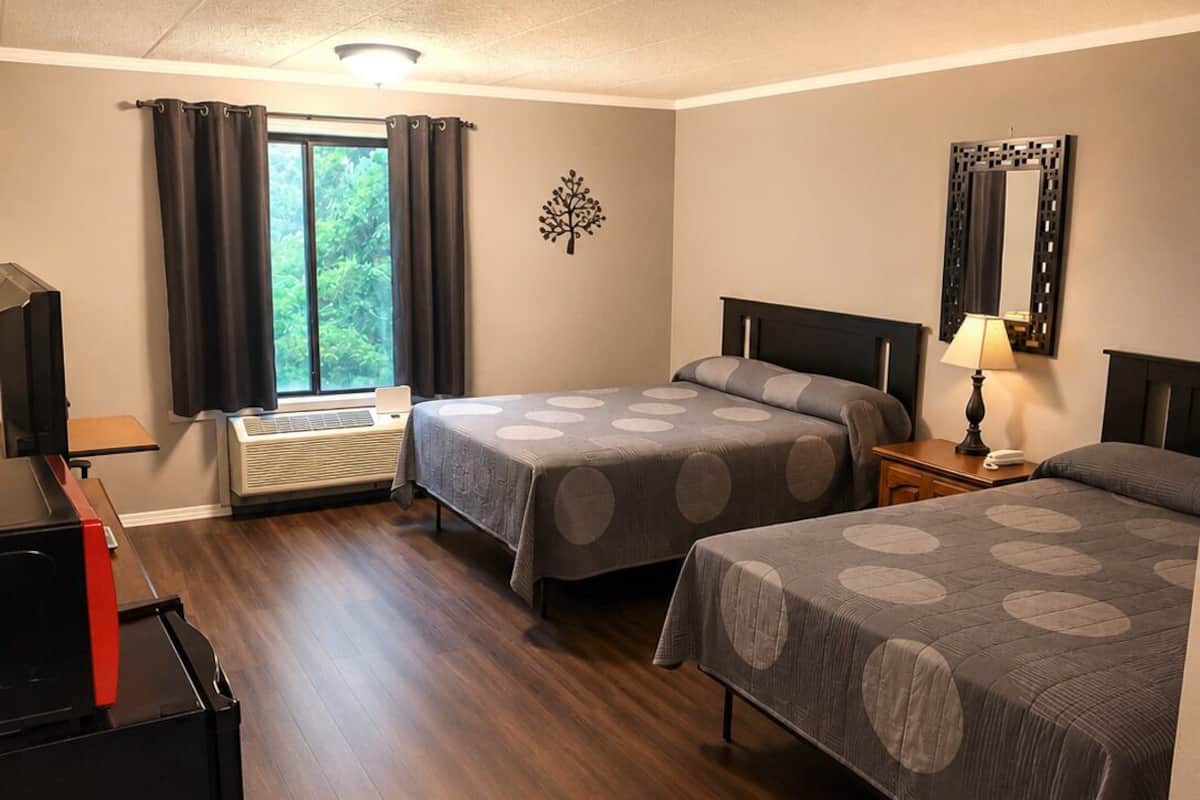 Habitación de hotel con dos camas, un escritorio, un televisor y una ventana con cortinas.