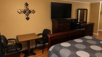 A hotel room with a bed, a desk, two chairs, a dresser, a television, and a wall-mounted decorative piece.