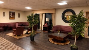 Um saguão de hotel com áreas de estar, uma mesa de centro, plantas em vasos e um espelho na parede.