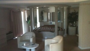 Quarto de hotel com cama, duas poltronas, uma mesinha e um espelho.