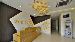A reception desk with a modern design, featuring a wooden counter and a wall with zodiac symbols. - Zodiak Kebonjati by KAGUM Hotels (Bandung)