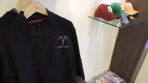 A black jacket with a 'ZODIAK' logo on a hanger, a shelf with hats, and a package of items on a lower shelf. - Zodiak Kebonjati by KAGUM Hotels (Bandung)