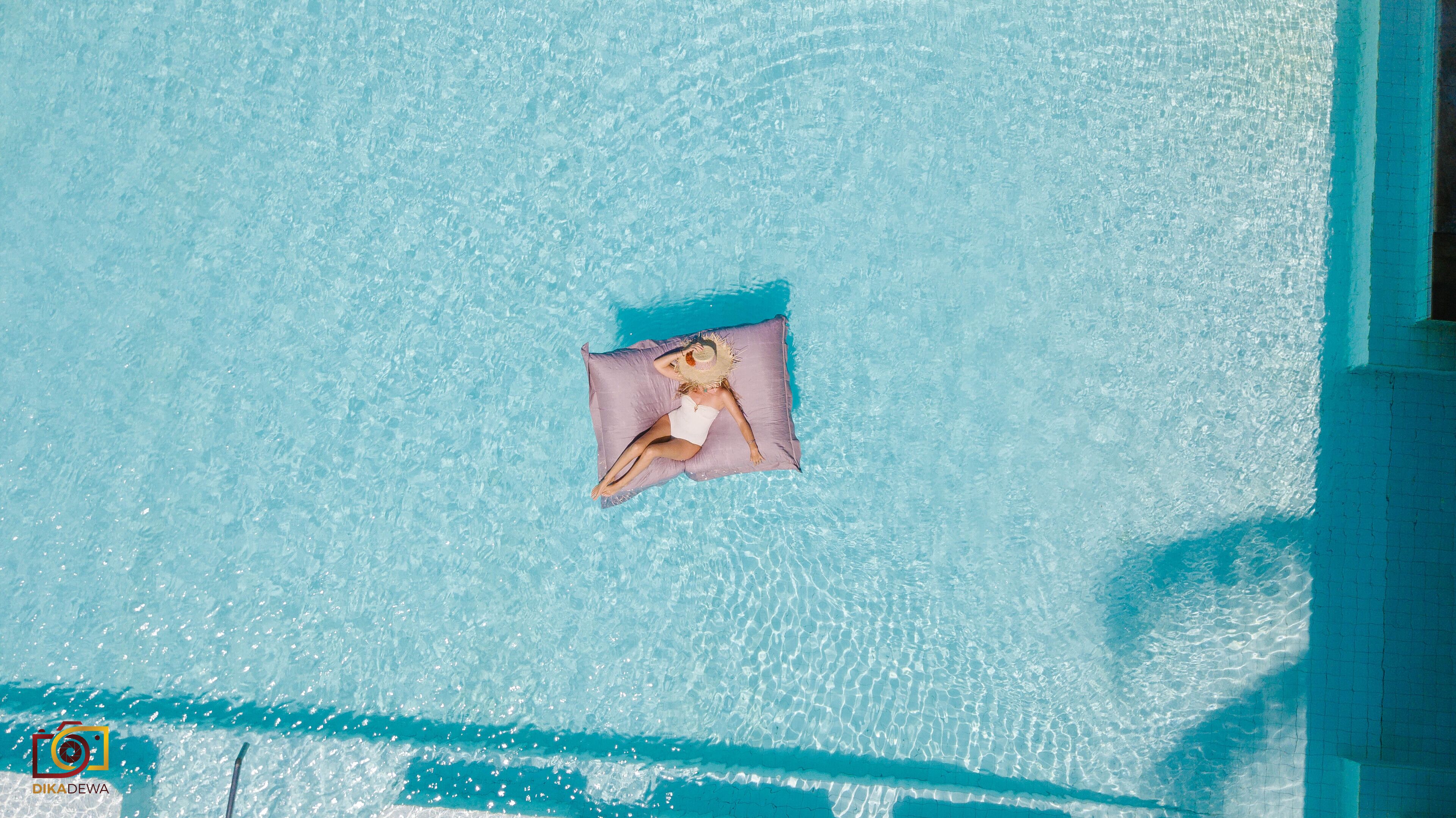 A clear blue pool with a person lying on a purple float.