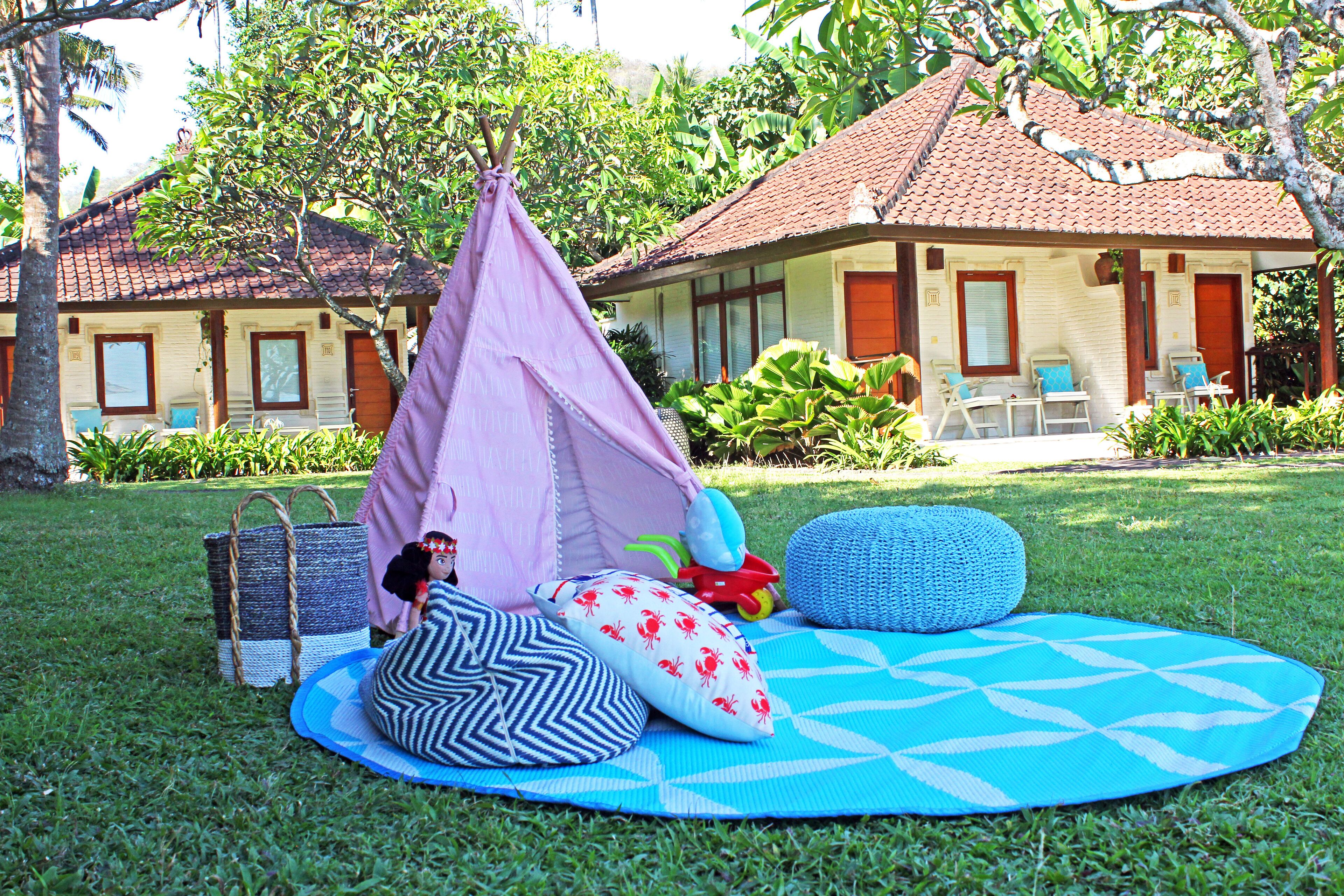 A grassy area with a tent, a mat, and a building with a tiled roof.