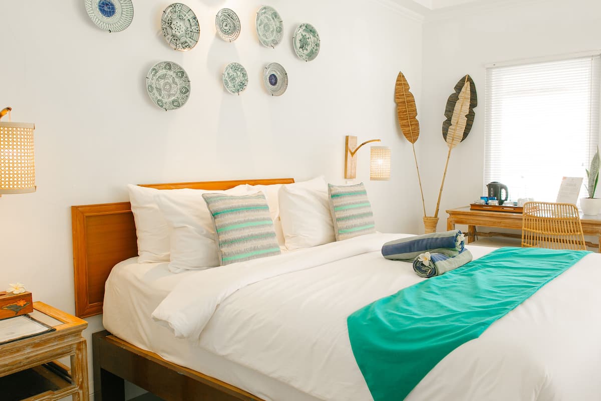 A neatly arranged bedroom with a wooden bed, white bedding, and decorative plates on the wall.