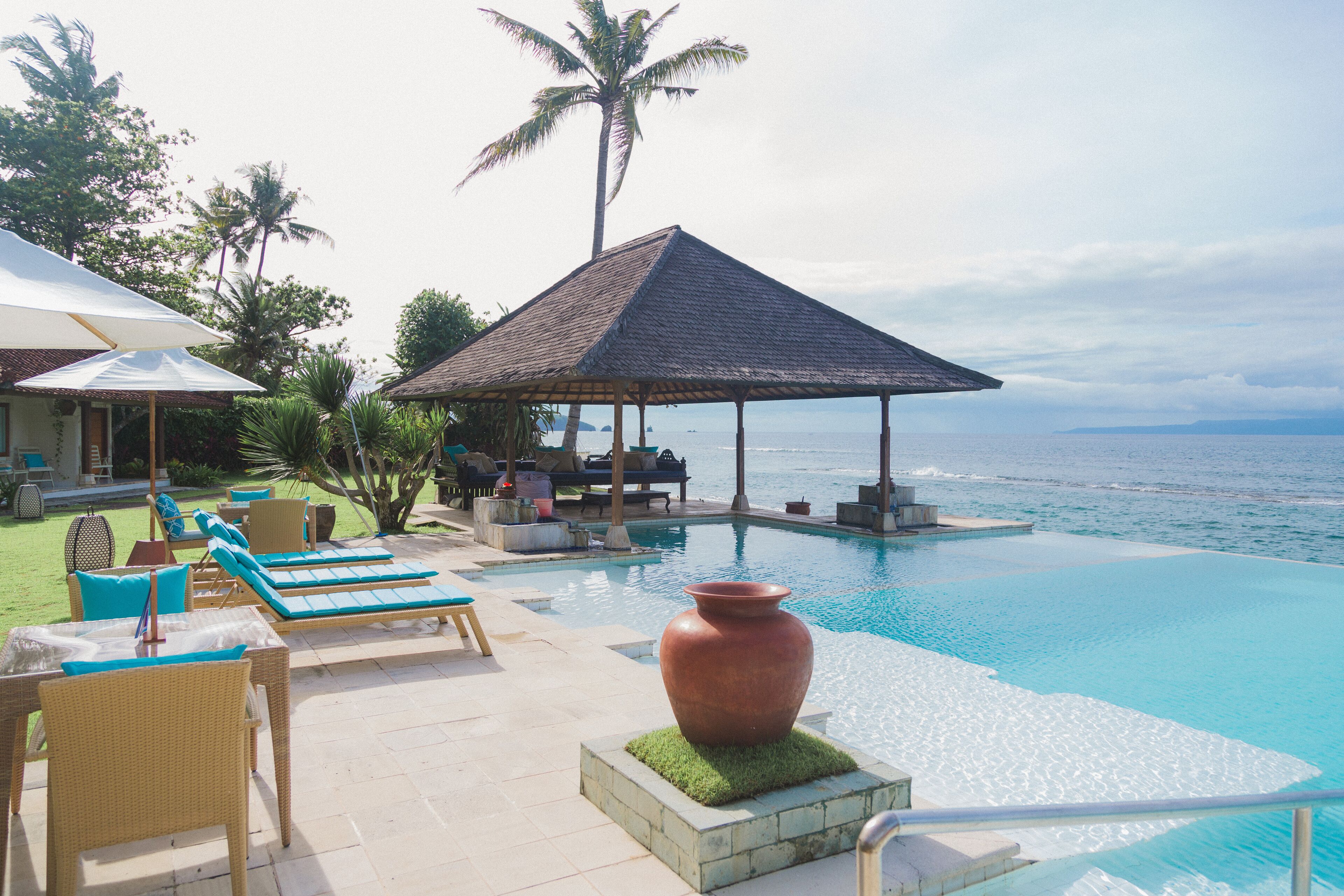 A resort pool area with lounge chairs, a large planter, and a gazebo overlooking the ocean.