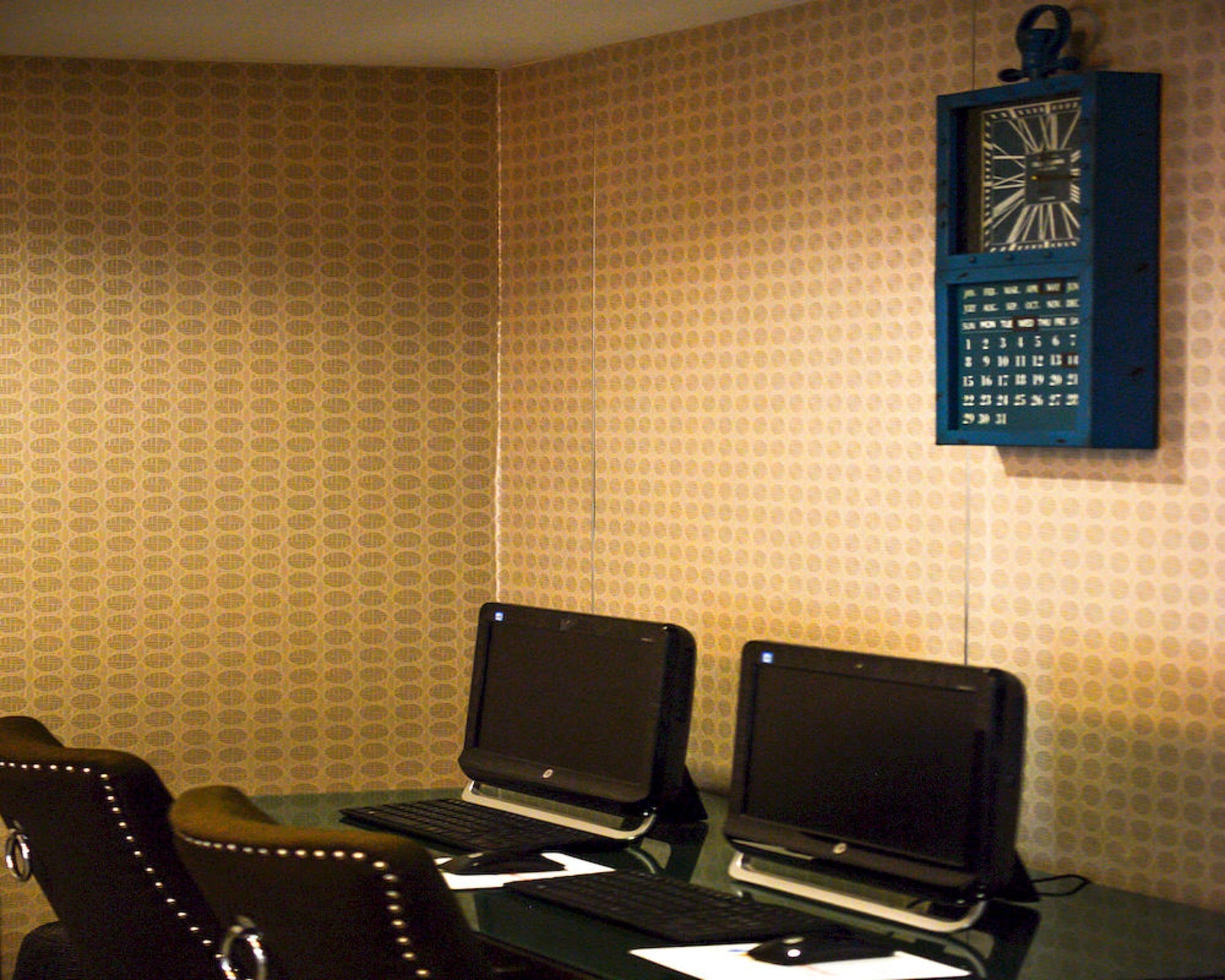 A room with two laptops on a desk, a clock on the wall, and patterned wallpaper.