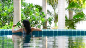 A person in a swimming pool with a tiled edge and lush greenery in the background. - iCheck Inn Residences Sathorn (Bangkok)