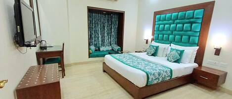 A hotel room with a large bed, a desk, a chair, a TV, and an air conditioning unit.
