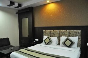 A hotel room with a bed, a nightstand, a chair, and a large mirror. - Hotel Blue Pearl (New Delhi)