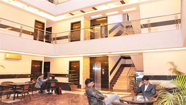 A spacious lobby with a central staircase, multiple seating areas, and a glass railing overlooking the lower level. - Hotel Blue Pearl (New Delhi)
