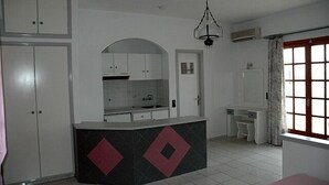 A kitchen with white cabinets, a central island with a black and red pattern, and a window with curtains. - La Luna (Hersonissos)