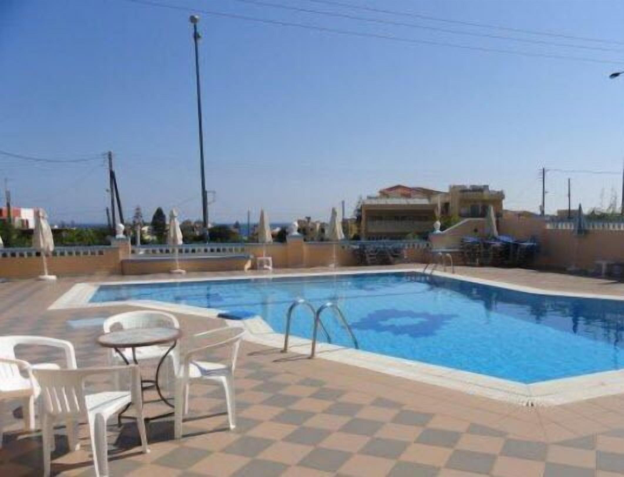 Une piscine dont le fond est recouvert de carreaux, entourée de chaises en plastique blanches et d’une table.