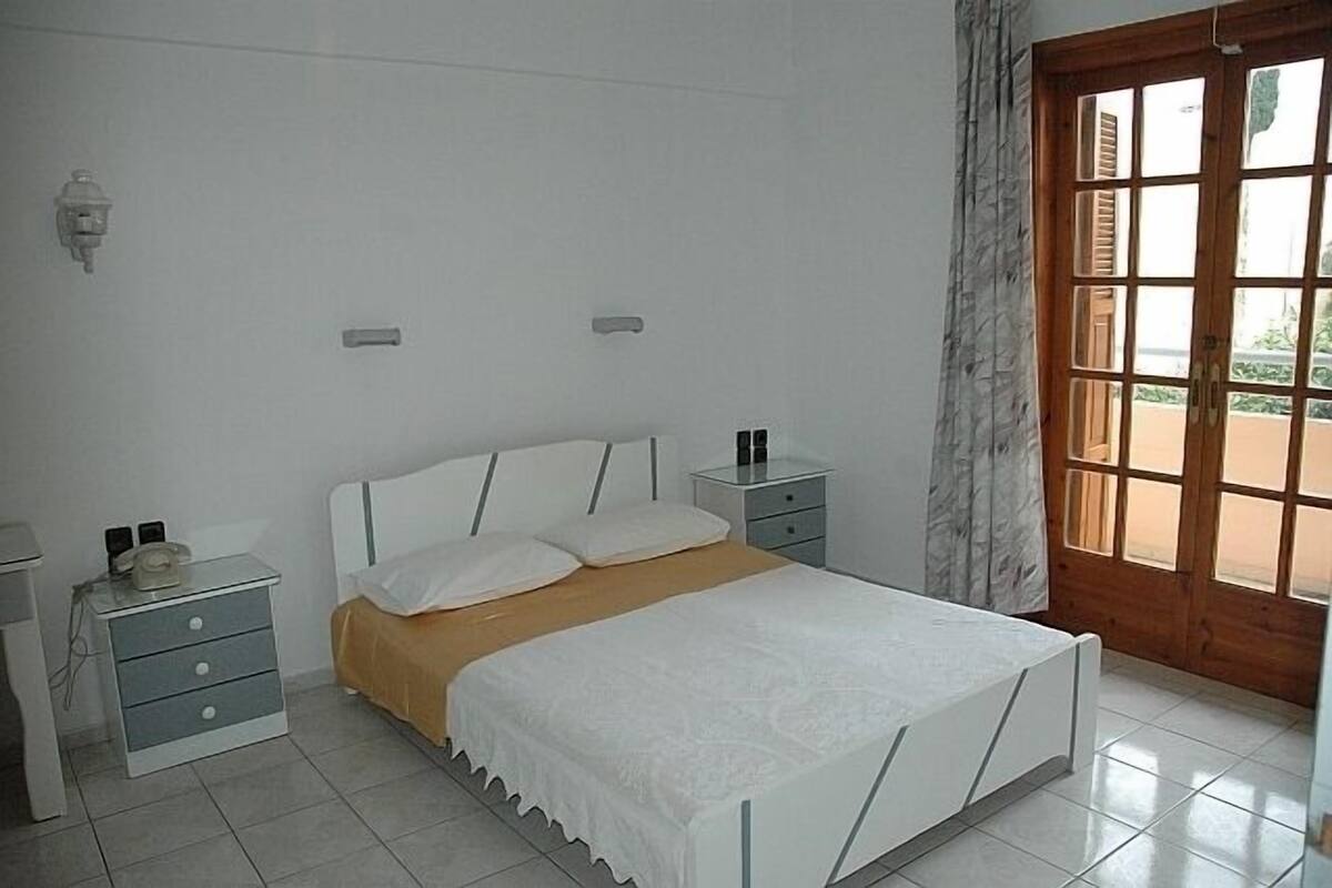 A bedroom with a bed, bedside tables, a nightstand, and a window with curtains.