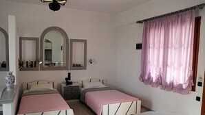 A bedroom with two beds, a nightstand, a mirror, and a window with curtains. - La Luna (Hersonissos)