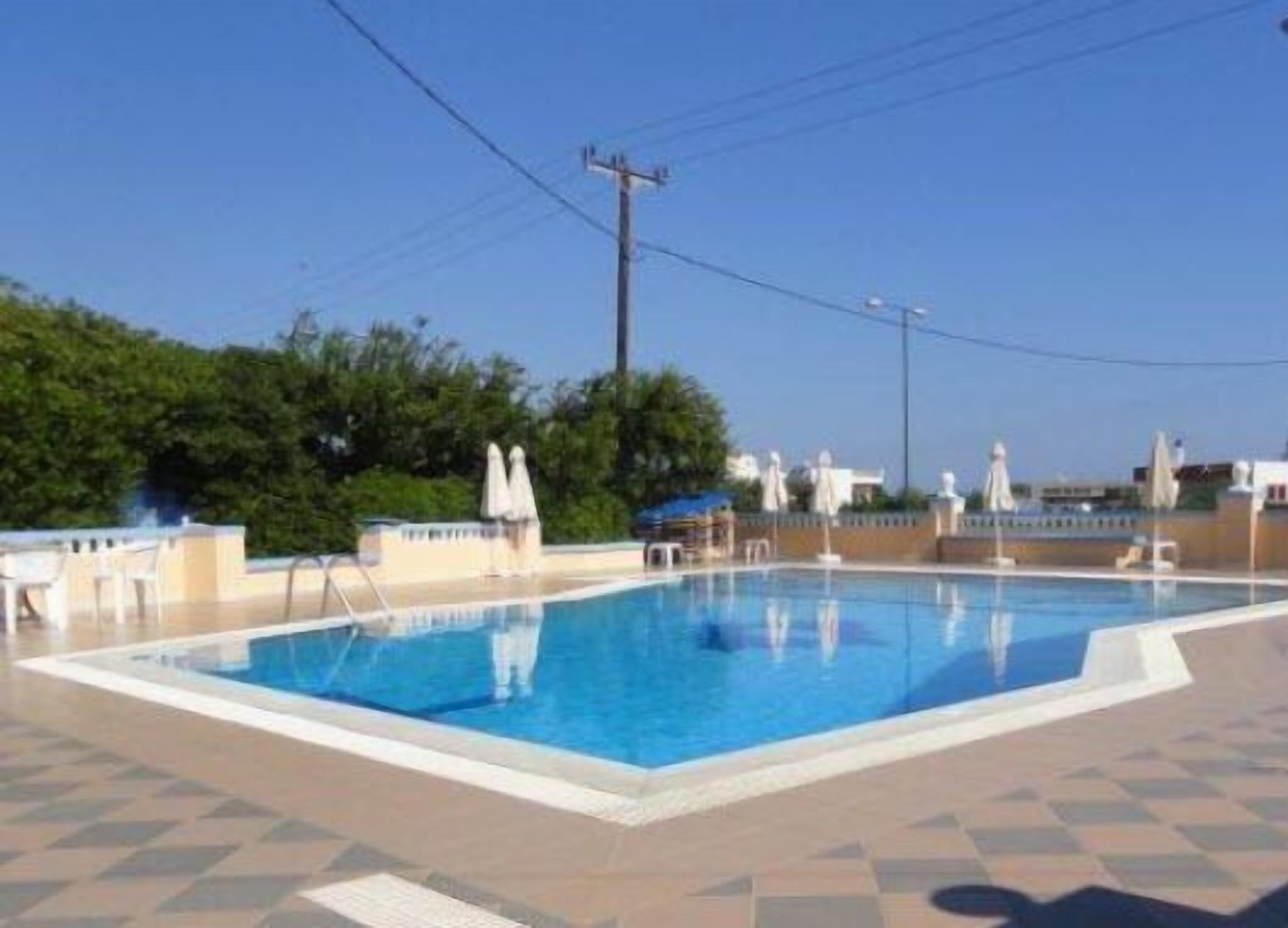 Une piscine dotée d’une terrasse carrelée, entourée de chaises longues et de parasols, avec un ciel dégagé en arrière-plan.