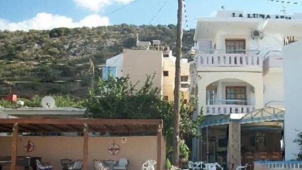 A swimming pool with lounge chairs and umbrellas, a building with balconies, and a hillside in the background. - La Luna (Hersonissos)