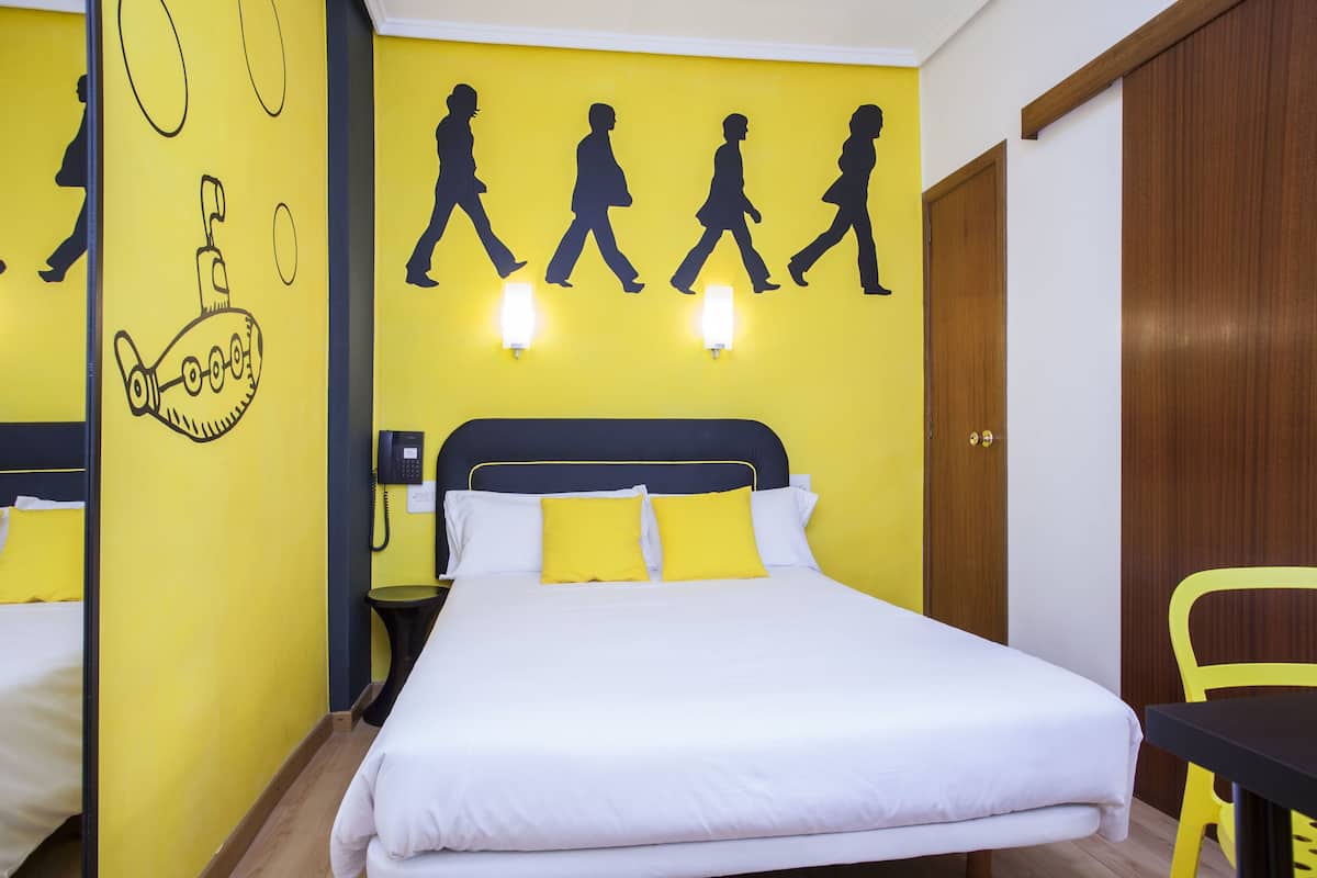 Een hotelkamer met een bed, nachtkastje, spiegel en een muur met silhouetten van mensen die lopen.