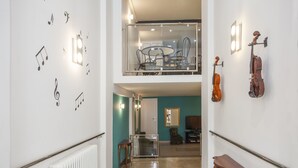 Un couloir avec un radiateur, une rambarde en verre, un banc en bois et un violon accroché au mur.