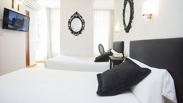 Une chambre d’hôtel avec deux lits, une télévision, un bureau avec une chaise et des miroirs décoratifs sur les murs.