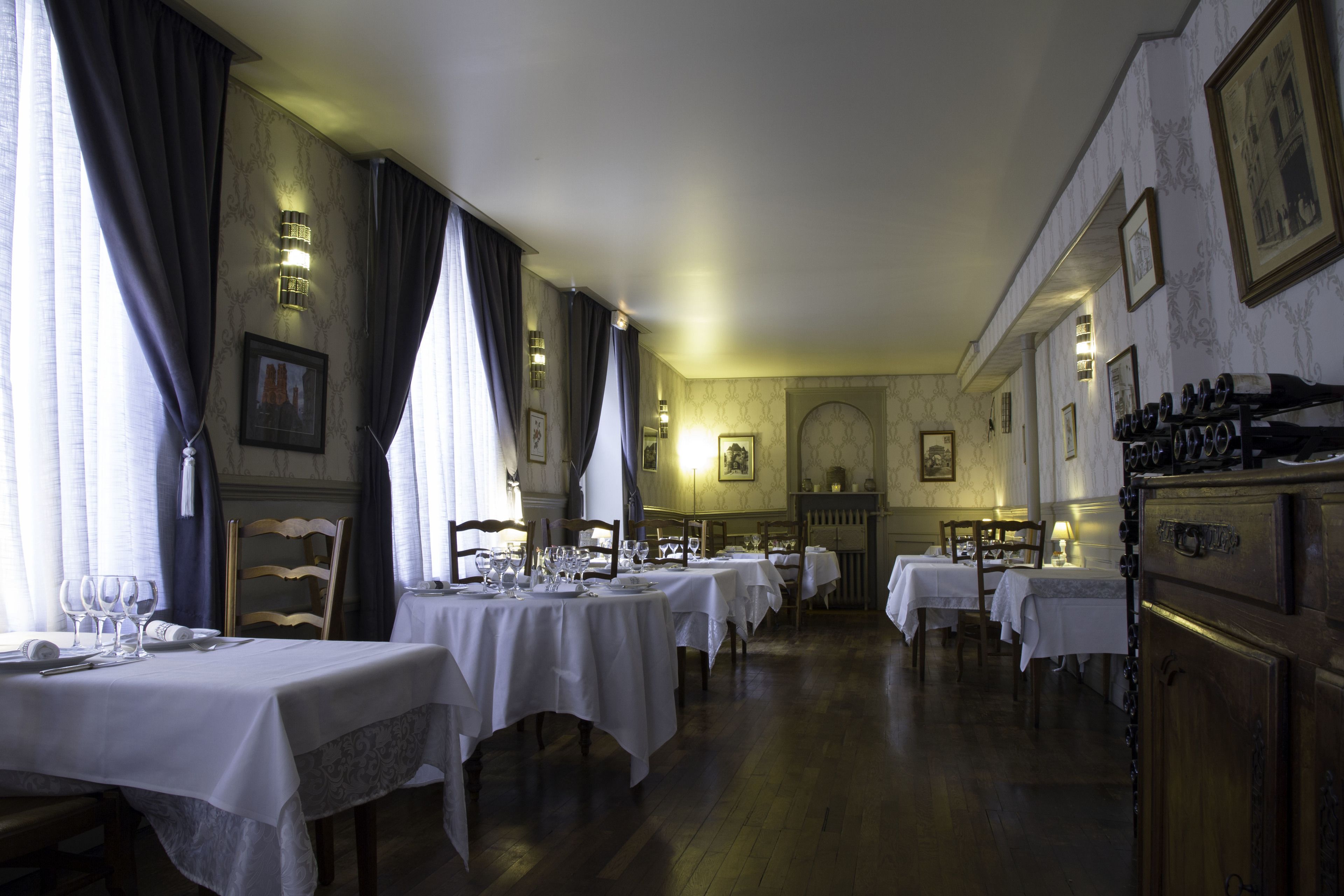 A dining area with multiple tables set for service, wooden chairs, and a chandelier.