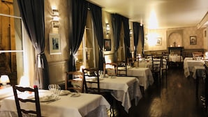 Un restaurante con varias mesas, cortinas oscuras y luces fijadas a la pared.