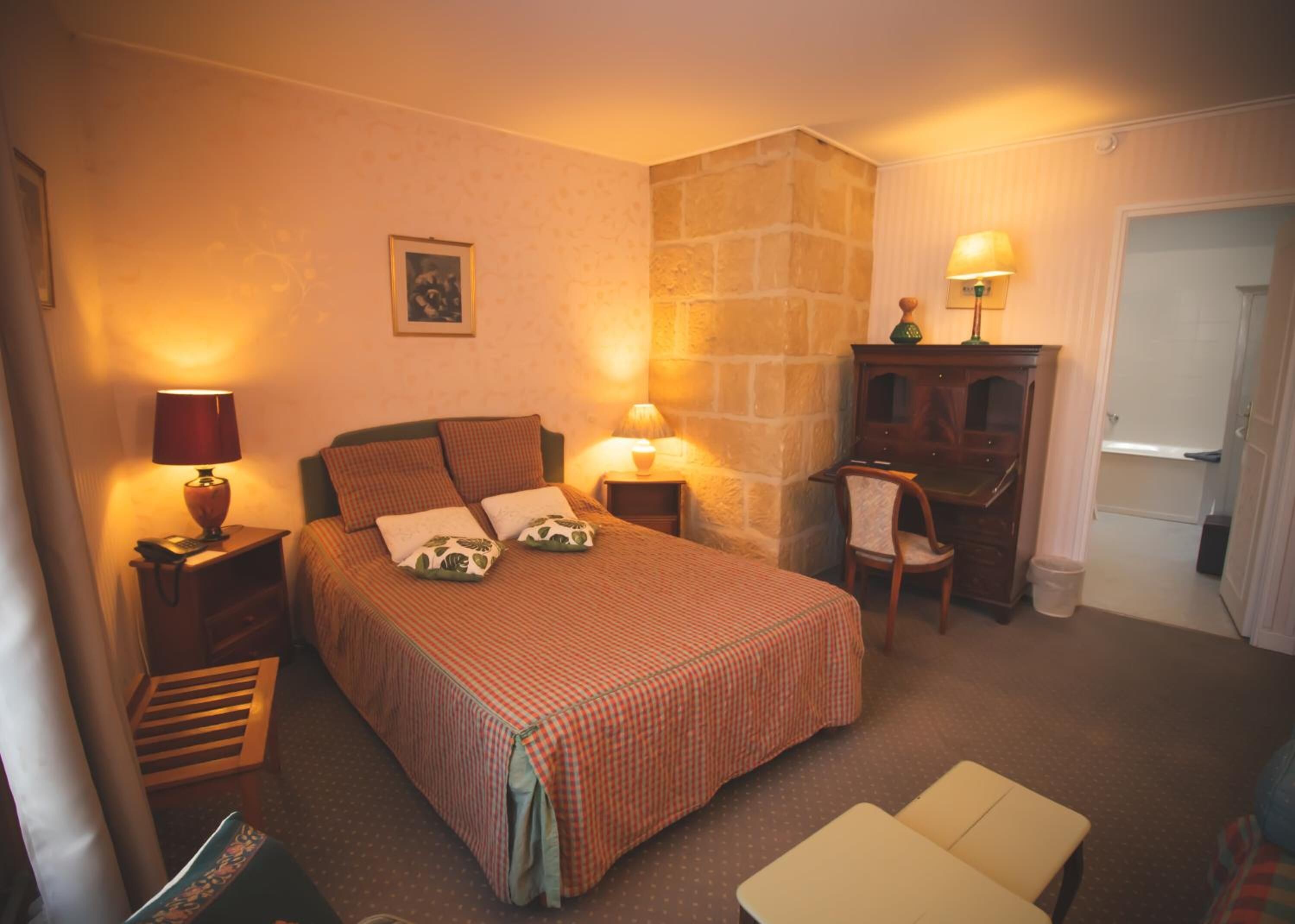 Ein gemütliches Hotelzimmer mit einem großen Bett, zwei Nachttischlampen, einem Schminktisch, einem Sessel und einem kleinen Tisch.